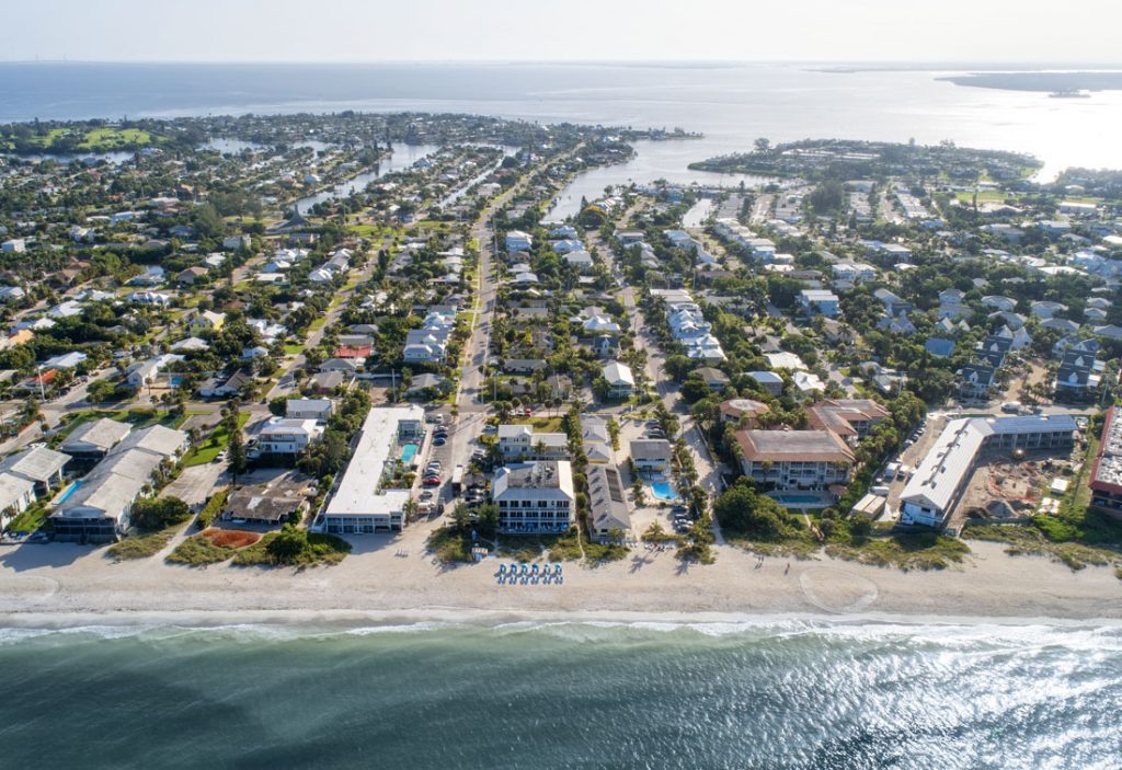 Aerial view of a coastal town and beachfront resort on a narrow strip of land between the ocean and a bay.